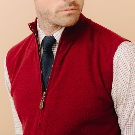 Close up of male model stood with arms behind back wearing Welbeck Geelong Wool Zip Up Gilet in Claret on plain cream background