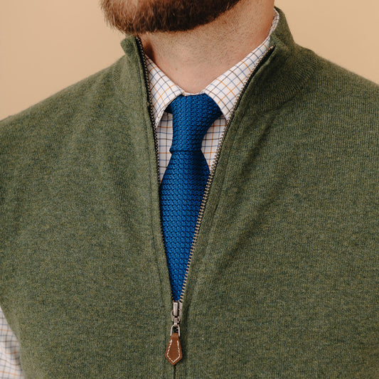 Male model wearing the Welbeck Geelong Wool Gilet  in Hunter Green over a checked shirt and royal blue tie stood against a cream background