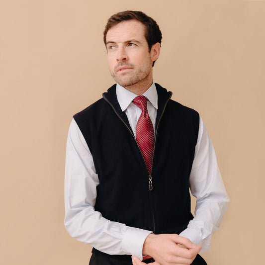 Male model stood wearing Welbeck Geelong Wool Zip Up Gilet in Navy over white shirt  and red tie against a cream plain background
