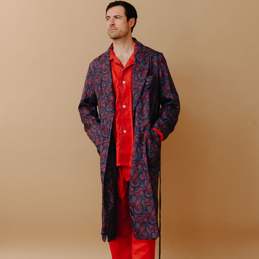 Model stood wearing Men's Fine Twill Cotton Pyjamas in Cardinal Red with madder silk paisley dressing gown on a plain cream background