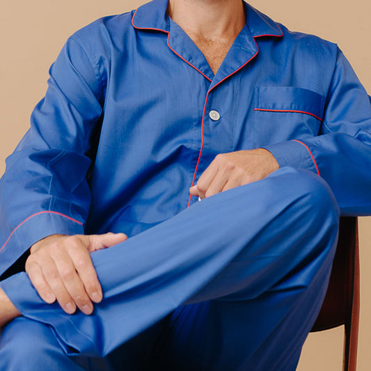 Close up image of male model sat on chair against cream background wearing Men's Fine Twill Cotton Pyjamas in Royal Blue