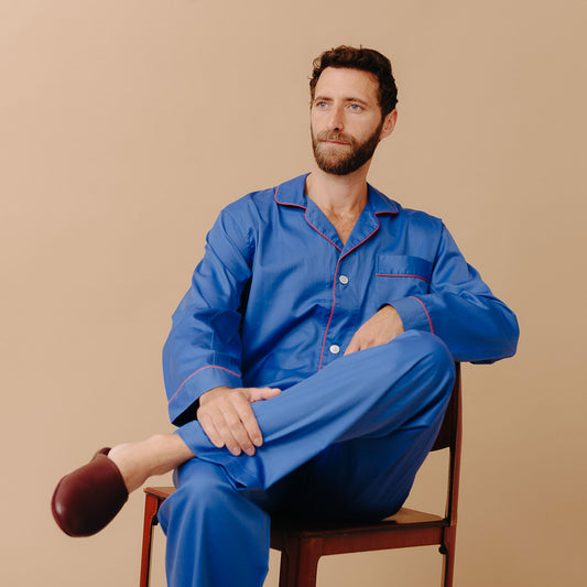 Male model sat on chair against cream background wearing Men's Fine Twill Cotton Pyjamas in Royal Blue
