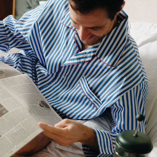 Male model laid on bed reading the newspaper wearing Men's Sea Island Quality Stripe Nightshirt in Royal Blue
