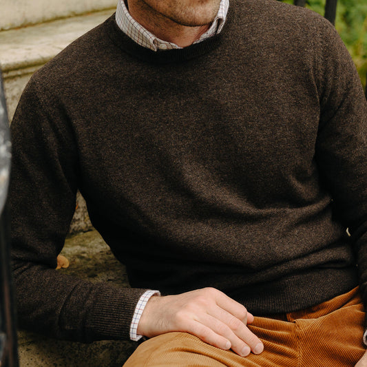 Close up image of male model sat outside on steps wearing Alston Cashmere Crew Neck Jumper in Pepperpot brown grey with orange cord trousers
